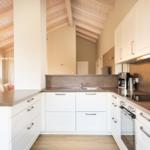 Küche mit weißen Schränken, dunklem Arbeitsplatz und Holzdecke.
