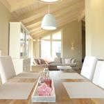 Essbereich mit Holztisch, weißen Stühlen und Blick in Wohnzimmer mit Sofa.