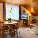 Wohn- und Essbereich mit Holztisch, Sofa und Fernseher unter Holzdach.