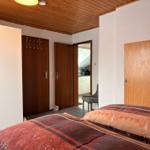 Schlafzimmer mit Bett, Holzdecke und Türen. Blick in die Küche.