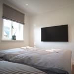 Schlafzimmer mit Bett, Fernseher und Fenster mit Rollladen.