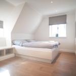 Schlafzimmer mit Doppelbett, Holzboden und Fenstern mit Rollläden.