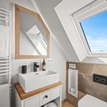 Badezimmer mit Dachschrägen, Waschbecken, Spiegel und Dachfenster.