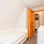 Schlafzimmer mit Einzelbett, Holztür und weißen Möbeln.