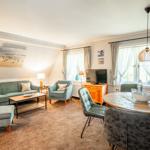Wohn- und Essbereich mit Sofa, Stühlen und Tisch. Fenster mit Vorhängen und Deckenlampe.