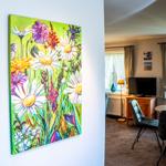 Ein großes Wandbild mit Blumen hängt in einem Wohnbereich mit Essplatz und TV.
