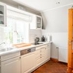 Küche mit weißen Schränken, Fenster und Holztür.