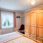 Schlafzimmer mit Holzschrank, Bett und Fenster mit Gardinen.