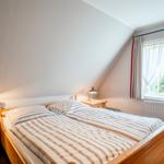 Doppelbett mit Streifenbettenlaken, zwei Nachttische mit Lampen und Fenster mit Vorhängen.