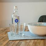 Holztisch mit Wasserglas, Flasche und Keramikschale.