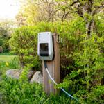 Ladestation im Garten an Holzpfosten mit Kabel und Grünflächen