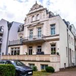 Historisches Gebäude mit Balkonen und Fenstern. Autos parken vor dem Haus.