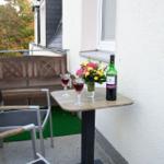 Terrasse mit Tisch, Stühlen, Blumen und Weinflasche. Blick auf Bäume und Hauswand.