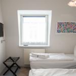 Zimmer mit zwei Betten, Fenster, TV und Handtuchständer.