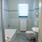 Badezimmer mit Badewanne, Toilette und Waschbecken. Fenster mit Jalousie und Heizkörper.