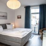 Schlafzimmer mit Bett, TV und Balkon. Dunkelblaue Vorhänge und Wandbilder.