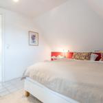 Bedroom with sloped ceiling, bed with colorful pillows, and door to bathroom.