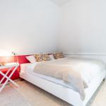 Bedroom with white bed, red wall, and small table.
