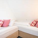 Two beds with white sheets and red pillows under sloped walls.