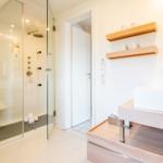 Shower with glass enclosure, sink, and wooden shelves on the wall.