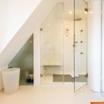 Shower with glass enclosure, toilet, and window under sloped ceiling.