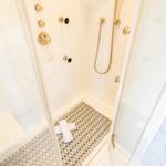 Shower with glass door, gold handles, and tiled floor.
