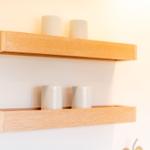 Two wooden shelves on the wall with white cylinders.