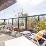 Terrace with table, chairs, and seating. View of greenery and lighthouse.