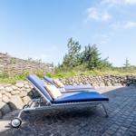 Two blue lounge chairs on cobblestone beside stone wall and wooden fence.