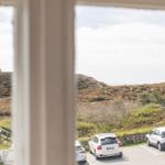 View through window onto parking lot with cars and hillside landscape.