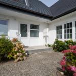 Weiße Villa mit Eingangstür und Blumenbeeten im Vorgarten.