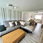 Wohnzimmer mit Sofa, Couchtisch und Essbereich im Hintergrund.