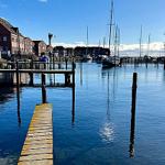 Hafen mit Booten und hölzernen Stegen unter blauem Himmel.