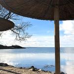 Strand mit Strohschirmen und Blick auf ruhiges Wasser unter blauem Himmel.
