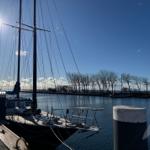 Segelboot liegt im Hafen, Sonne scheint, Wasser spiegelt den Himmel.