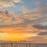 Sonnenuntergang über dem Wasser mit orangefarbenen Wolken am Horizont.