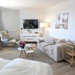 Wohnbereich mit Sofa, Fernseher und Schaukelstuhl. Holzboden und Wandbilder.