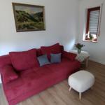 Ein Wohnzimmer mit rotem Sofa, grauen Kissen, weißem Hocker und Wandbild.