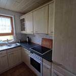 Küche mit Holzschränken, Induktionskochfeld und Fenster mit Vorhang.