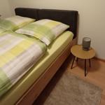 Ein Bett mit grün-weißem Bettzeug, Nachttisch und Fenster.