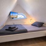 Schlafzimmer mit Dachschräge, Bett, Fernseher und Fenster.