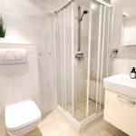 Bathroom with shower, sink and toilet. White tiles and mirror.