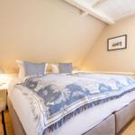 Schlafzimmer mit Dachschräge, Bett mit blau-weißem Deckenbezug und Fenster mit blau-weißem Rolladen.