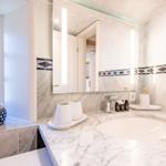 Badezimmer mit Marmorwaschtisch, beleuchtetem Spiegel und Fenster.
