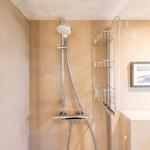 Dusche mit Duschbrause und Aufbewahrungskorb an der Wand