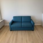 A blue sofa in the living room with wooden floor and window.
