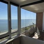 View of the sea through large windows and balcony with wooden deck.