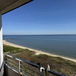 View from balcony over beach and sea under blue sky.