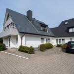 Modernes Haus mit Balkon, Dachfenstern und gepflastertem Hof. Ein Auto parkt vor der Tür.