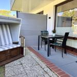Terrasse mit Strandkorb, Tisch und zwei Stühlen. Bodenbelag aus Stein und Teppich.